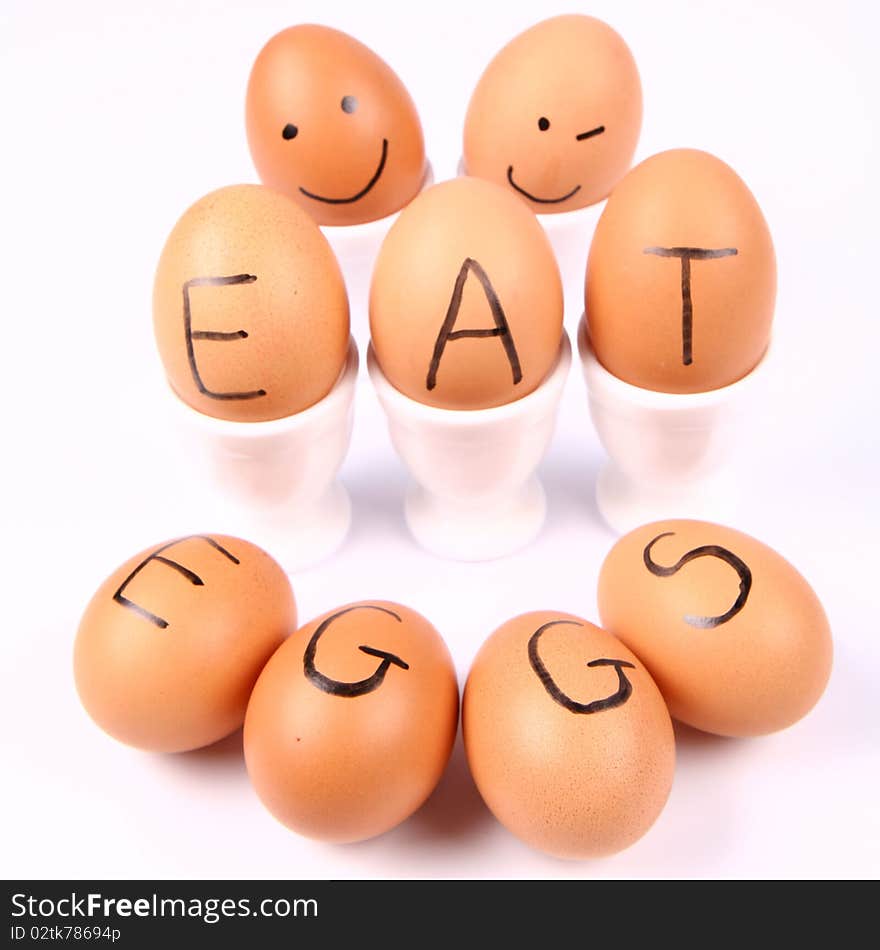 Eggs with an inscription EAT EGGS and eggs with smiling faces in an egg holders on white background