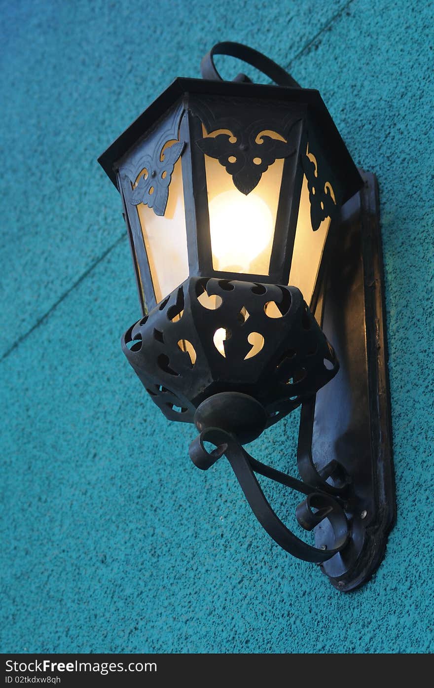 A black wrought iron lamp hangs on a blue wall. A black wrought iron lamp hangs on a blue wall