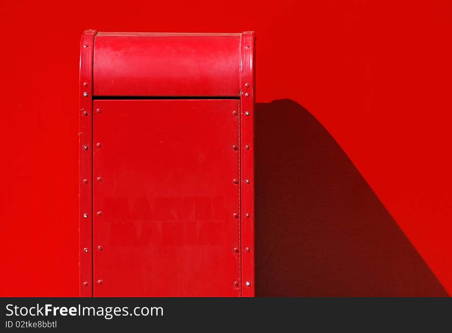 A red trash can with a dramatic shadow against a red wall