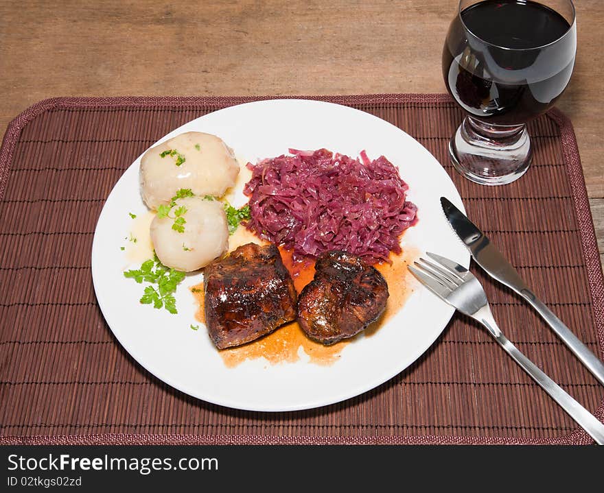 A studio shot a broiled pork tenderloin glazed with a rum and apple cider reduction served with steamed and peeled potatoes with red cabbage and a Shiraz. A hardy country fall meal served on a place mat on a rustic wooden table. A studio shot a broiled pork tenderloin glazed with a rum and apple cider reduction served with steamed and peeled potatoes with red cabbage and a Shiraz. A hardy country fall meal served on a place mat on a rustic wooden table.