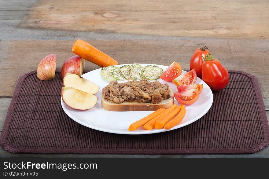 A studio shot of a plated pulled pork sandwich with a quatered apple, carrot, tomatoes and dried cucumber slices as garnishes. A harvest type lunch on a wooden rustic table. A studio shot of a plated pulled pork sandwich with a quatered apple, carrot, tomatoes and dried cucumber slices as garnishes. A harvest type lunch on a wooden rustic table.