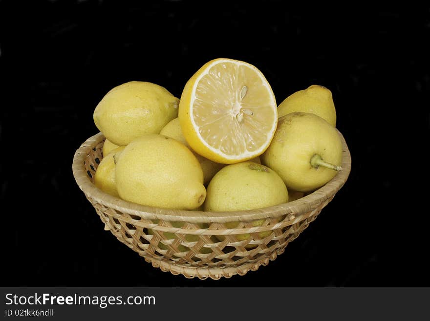 Fresh ripe lemons in wicker wooden vase in isolated over black