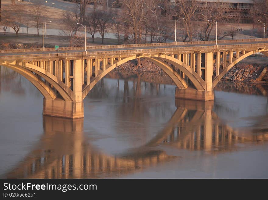 Photo of a bridge over a river as the morning sun shines on it causing a beautiful reflection.