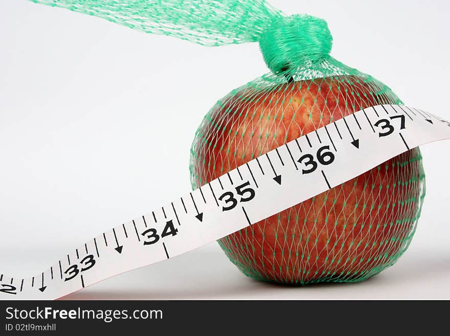 Concept shot of good health with an apple in a net and an inch tape with 36 inch in focus. Concept shot of good health with an apple in a net and an inch tape with 36 inch in focus