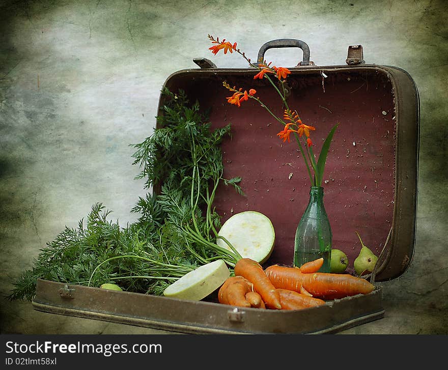 A carrot, pears, vegetable marrows and bottle with a flower, lies in an old suitcase. A carrot, pears, vegetable marrows and bottle with a flower, lies in an old suitcase