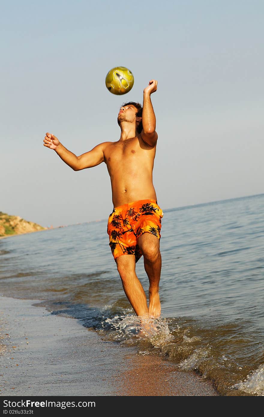 Handsome young man playing football on a sea shore. Handsome young man playing football on a sea shore