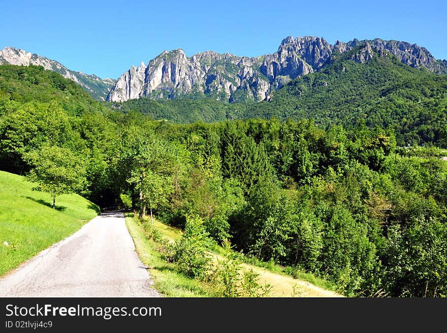 Narrow road traversing the mountain and going green a rocky peak in a blue sky. Narrow road traversing the mountain and going green a rocky peak in a blue sky