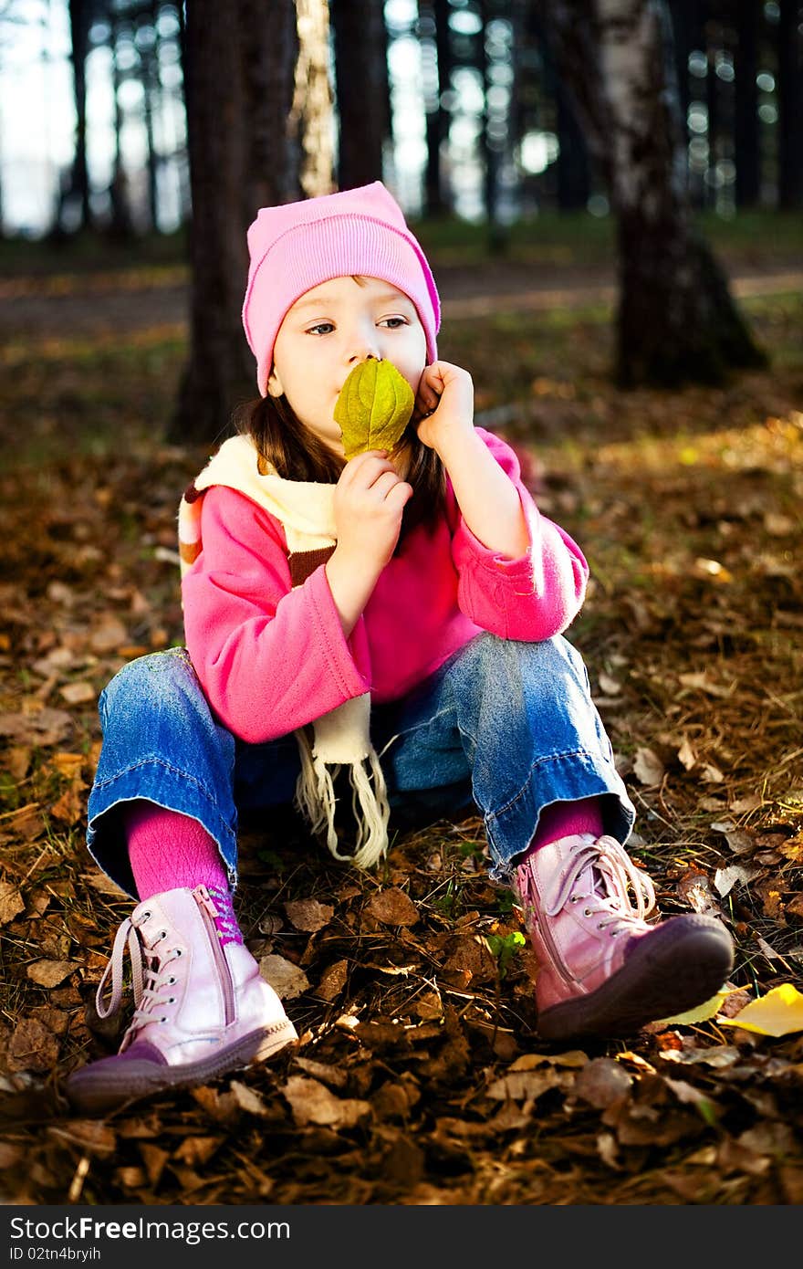 Cute thoughtful little girl on the grass in the autumn park. Cute thoughtful little girl on the grass in the autumn park