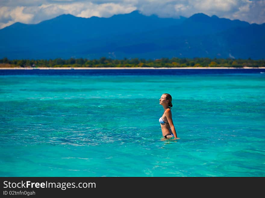 A beautiful woman wearing  white bikini facing the sea on a vacant beach in paradise