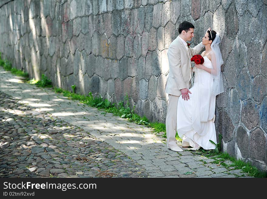 Bride in white dress and groom  near old wall. Bride in white dress and groom  near old wall