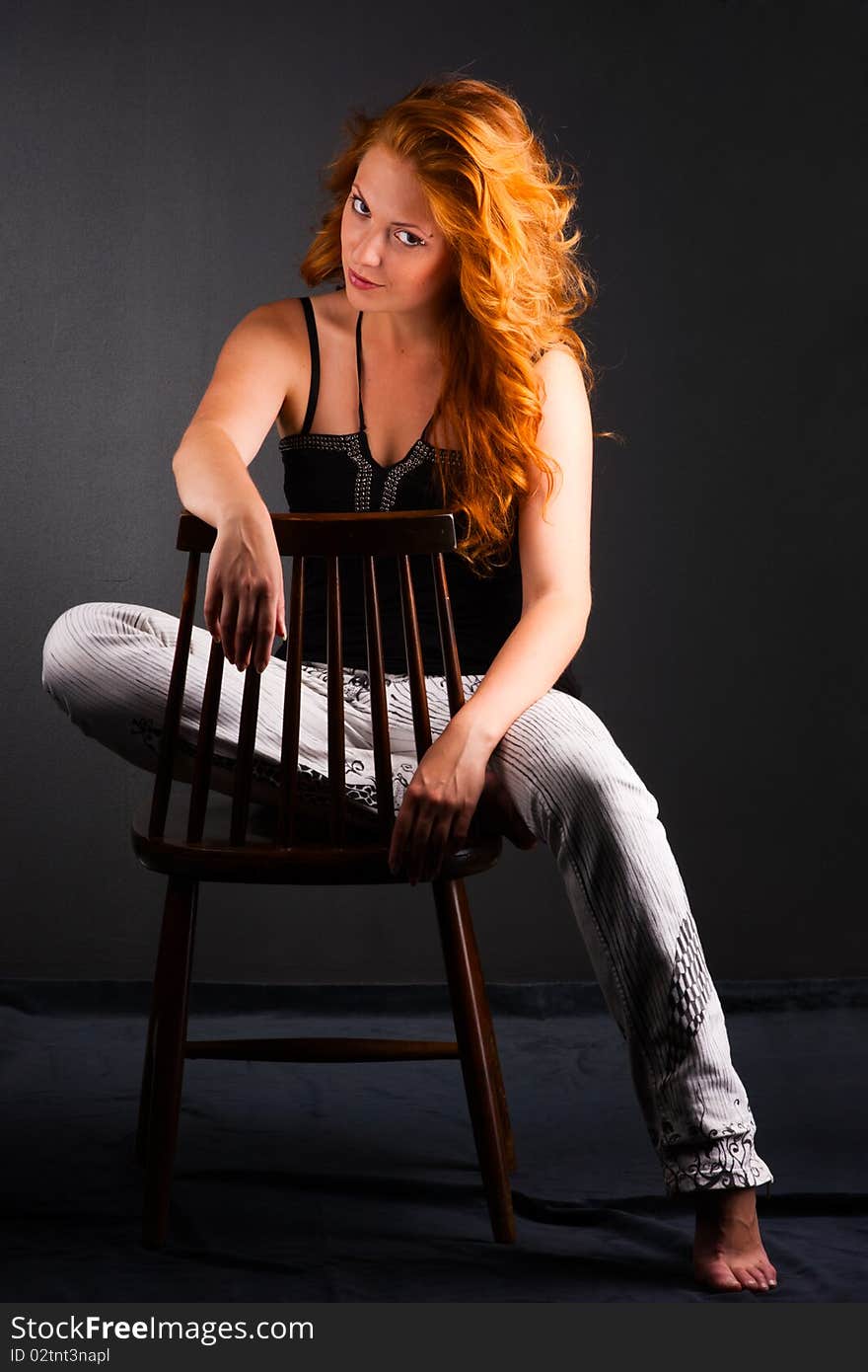 Portrait of a beautiful redheaded woman in a chair on a dark background. Portrait of a beautiful redheaded woman in a chair on a dark background