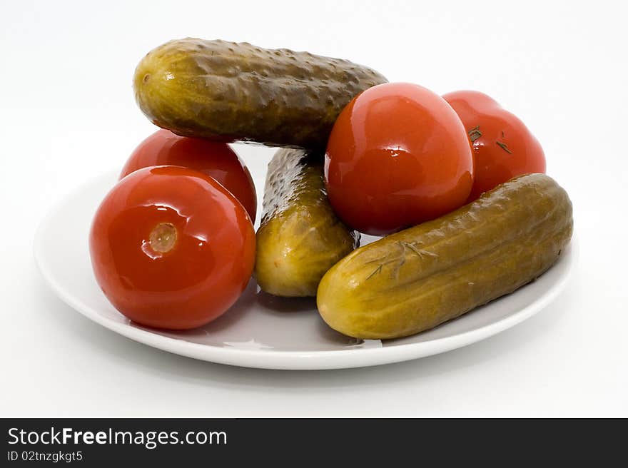 Homemade salted tomatos and cucumber on a plate on a white background. Homemade salted tomatos and cucumber on a plate on a white background