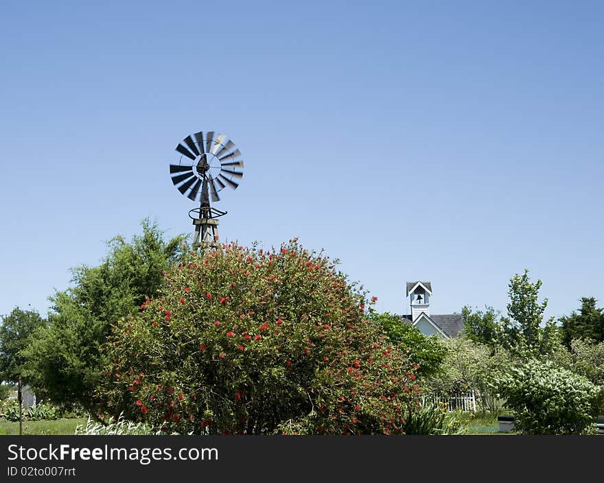 Top of windmill turning in the wind, with trees surrounding it and church in background