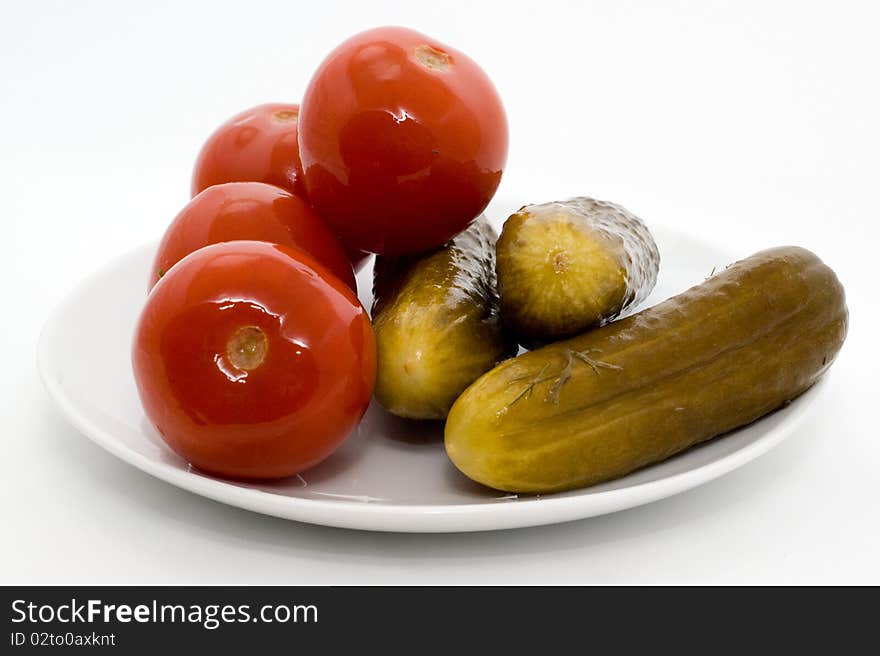 Homemade salted tomatos and cucumber on a plate on a white background. Homemade salted tomatos and cucumber on a plate on a white background