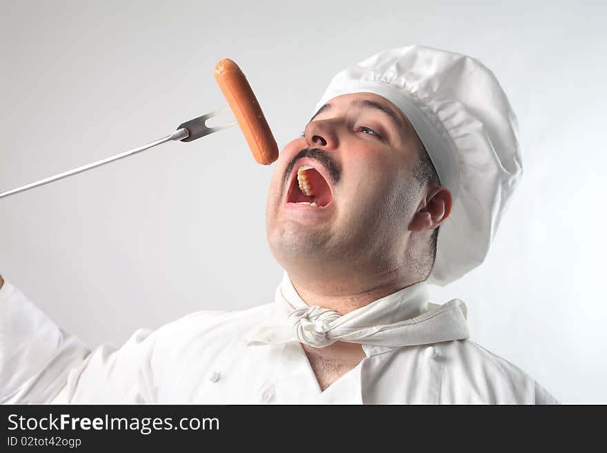 Cook eating a sausage from a fork. Cook eating a sausage from a fork