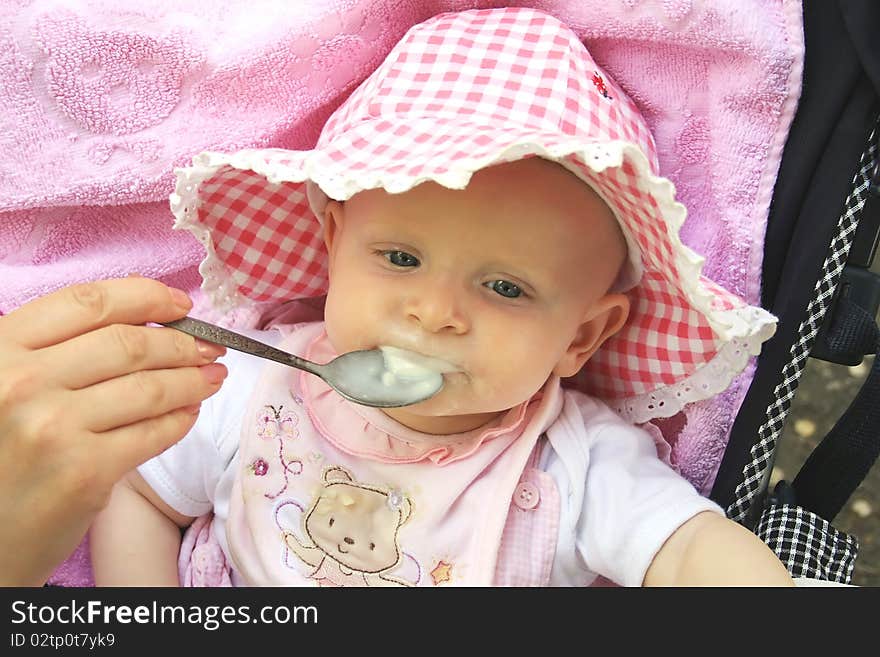 Little girl sits in a carriage and she is fed from a spoon. Little girl sits in a carriage and she is fed from a spoon