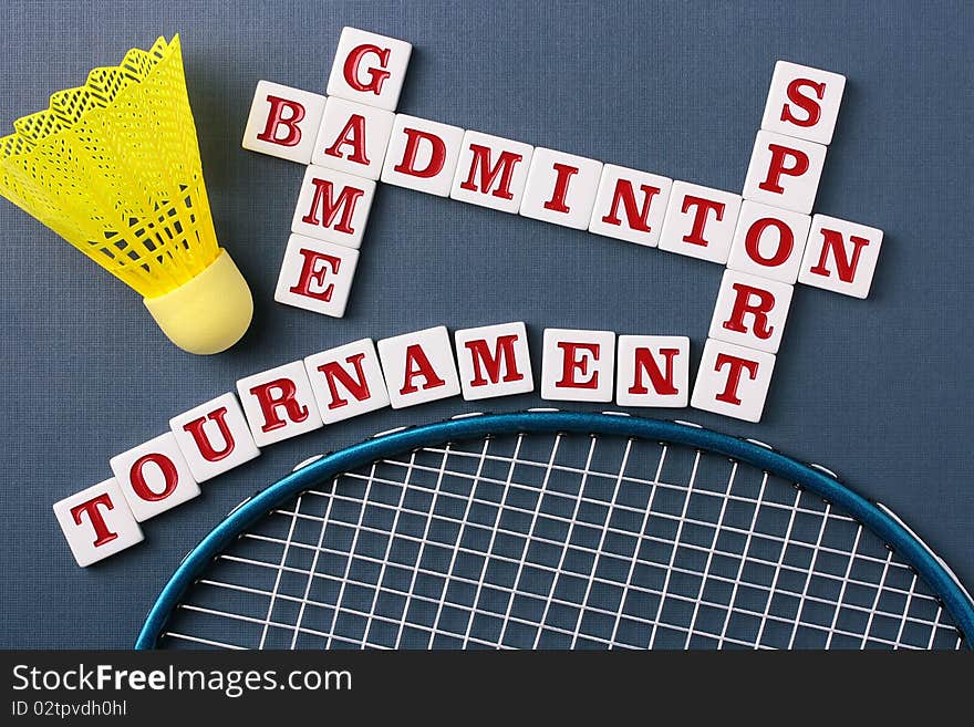 A yellow synthetic badminton shuttlecock next to a racquet and a badminton crossword.