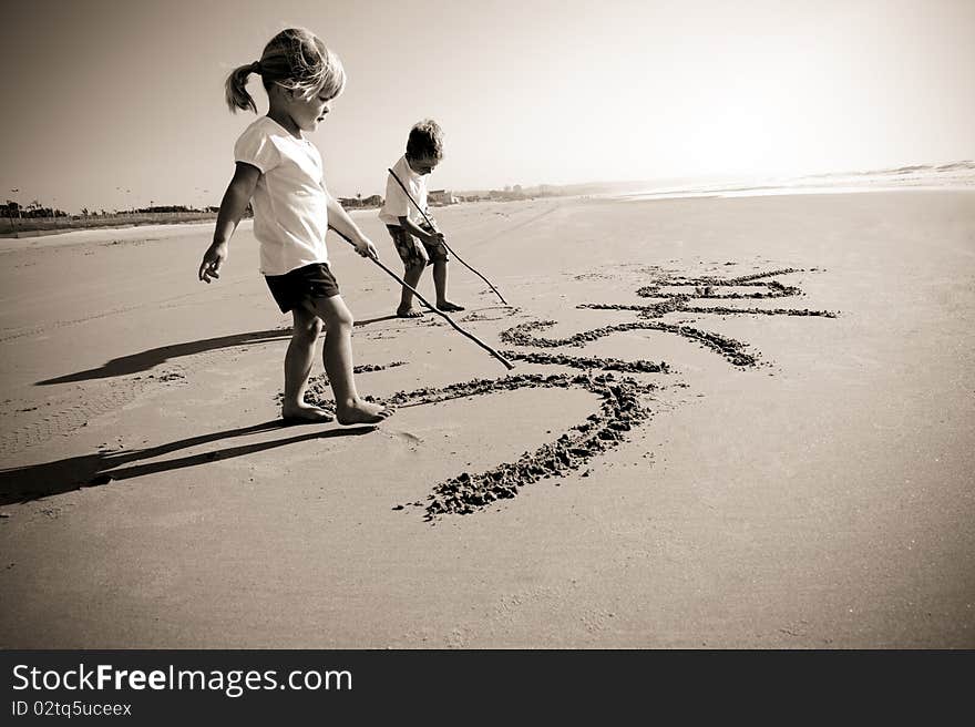 Lovely young brother and sister write words in the sand together. Lovely young brother and sister write words in the sand together