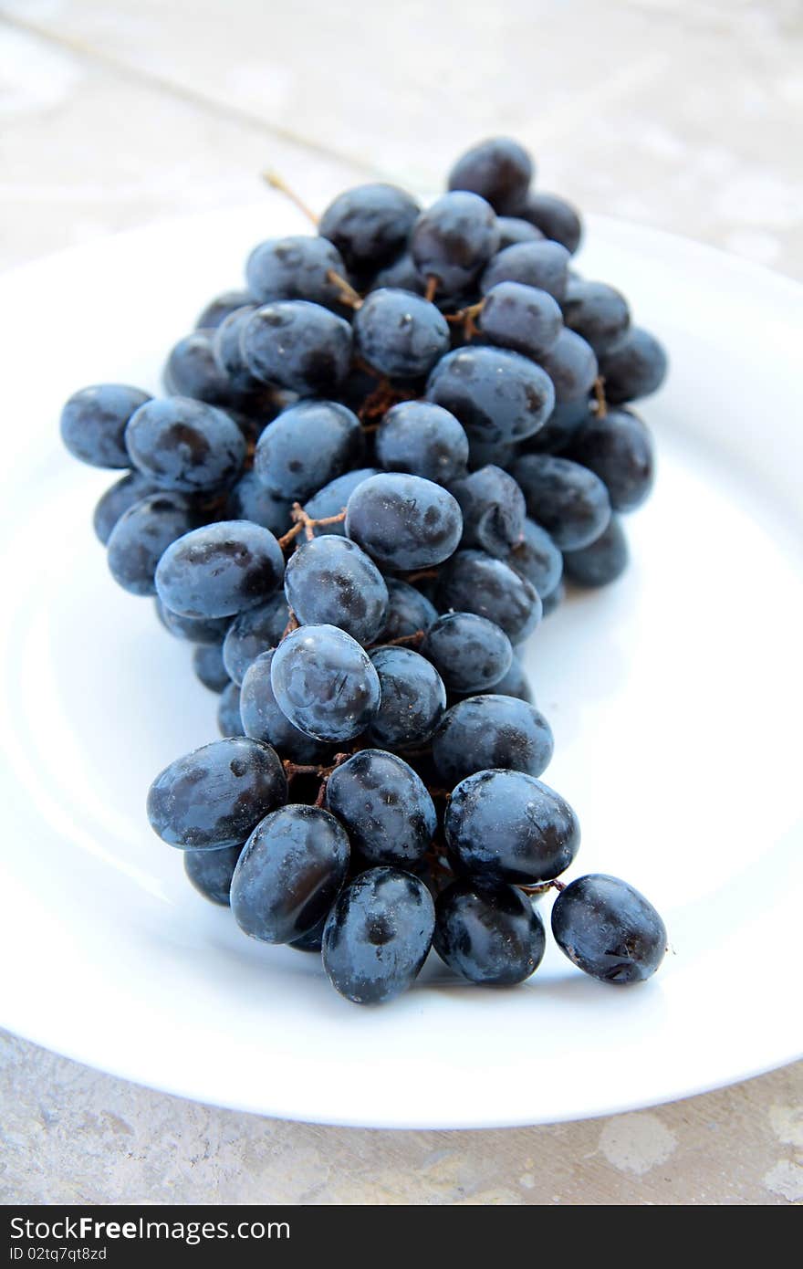 Black grapes on a white plate on the table