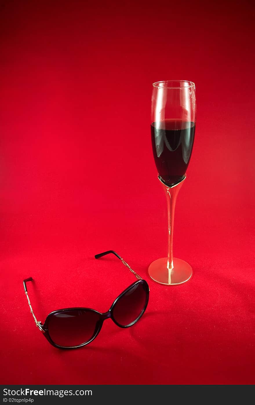 Wineglass with red dry wine and sunglasses on a red background. Wineglass with red dry wine and sunglasses on a red background.