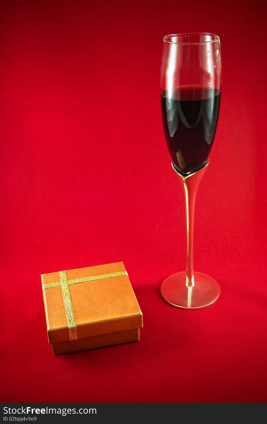 Elegant wineglass, red wine and gift box on red background. Elegant wineglass, red wine and gift box on red background