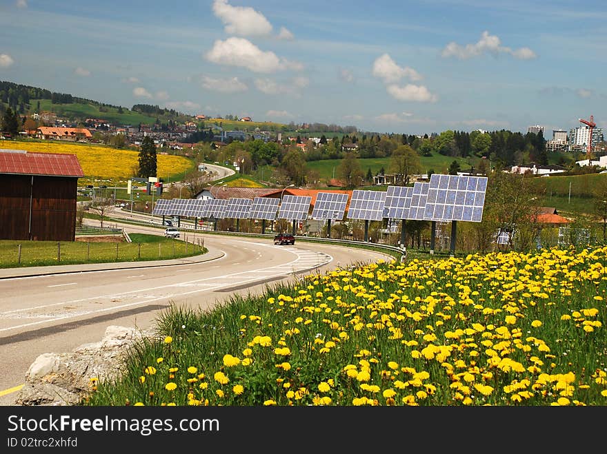 Solar cells along the roat to Le-Chaux-de-Fonds city, yellow flowers of dandelions at foreground. Solar cells along the roat to Le-Chaux-de-Fonds city, yellow flowers of dandelions at foreground