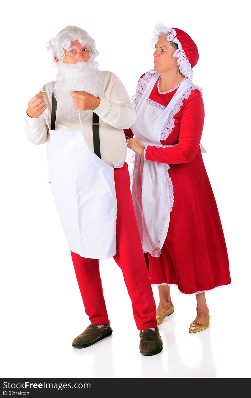 Mrs. Santa putting an apron on Santa Claus, who isn't looking any too pleased. Isolated on white. Mrs. Santa putting an apron on Santa Claus, who isn't looking any too pleased. Isolated on white.