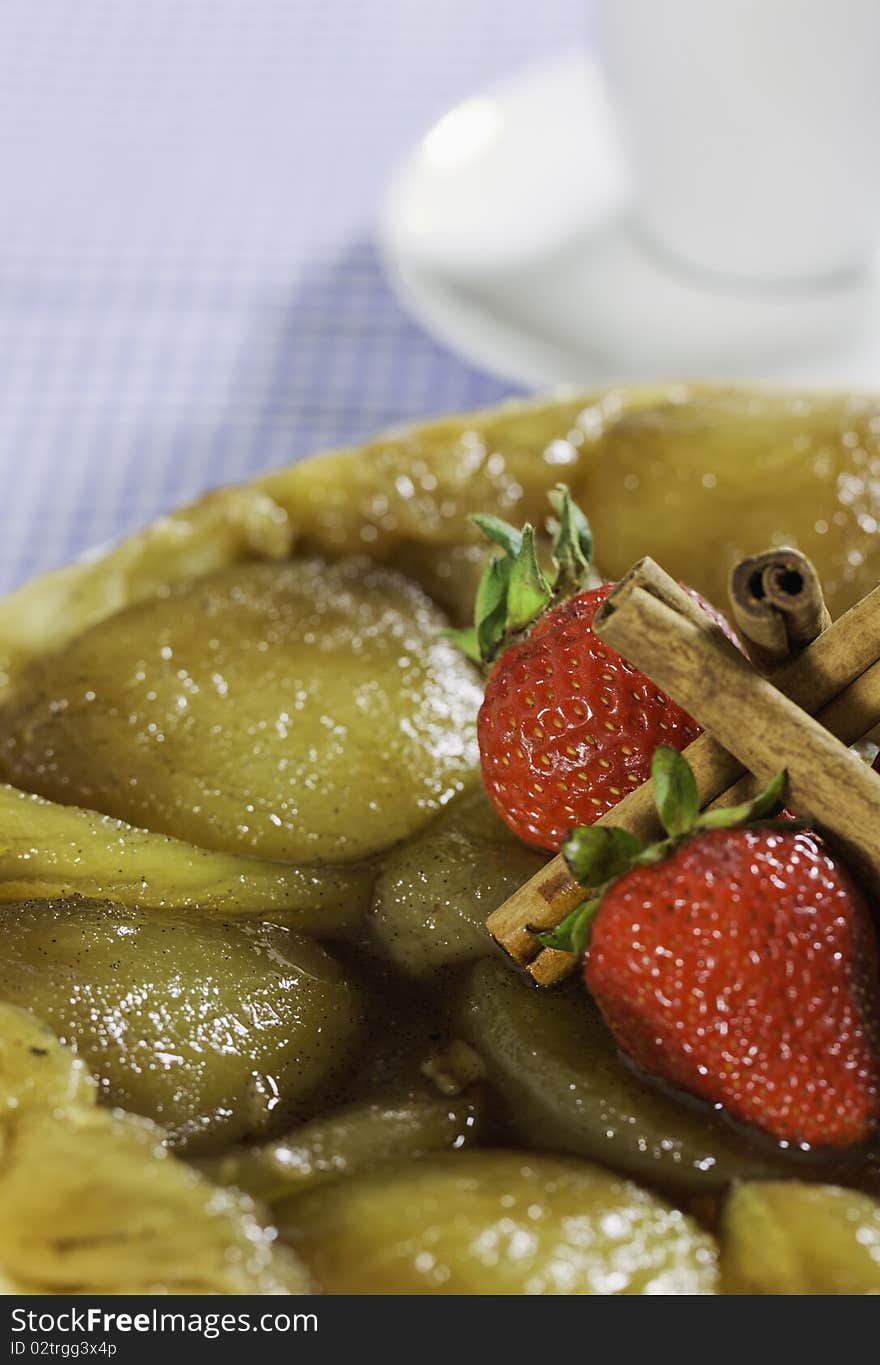 French style apple pie with stawberry and cinnamon on the top.Coffee cup in the background. Shallow depth of field.