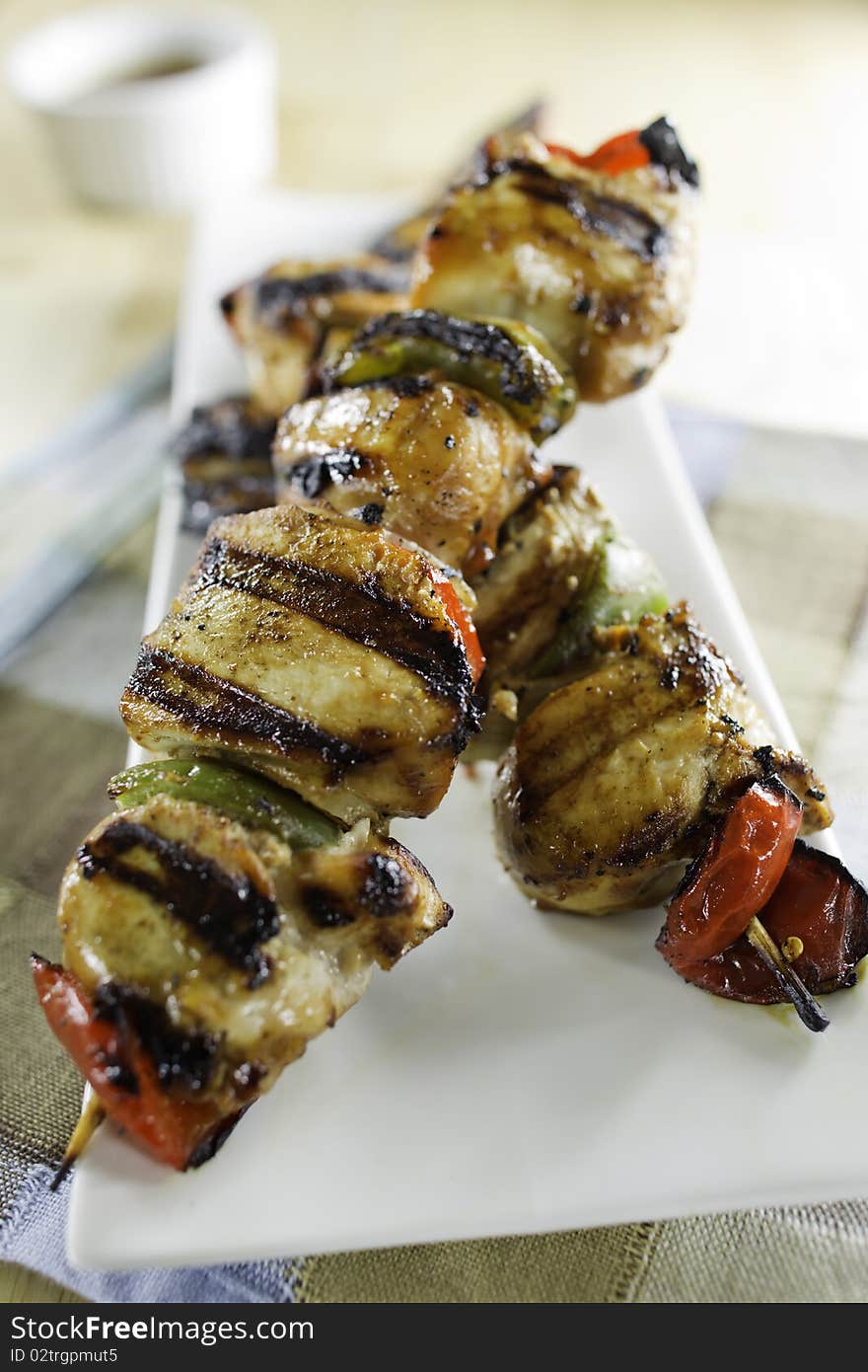 Grilled chicken skewers on a white plate with vegetables. Shallow depth of field.