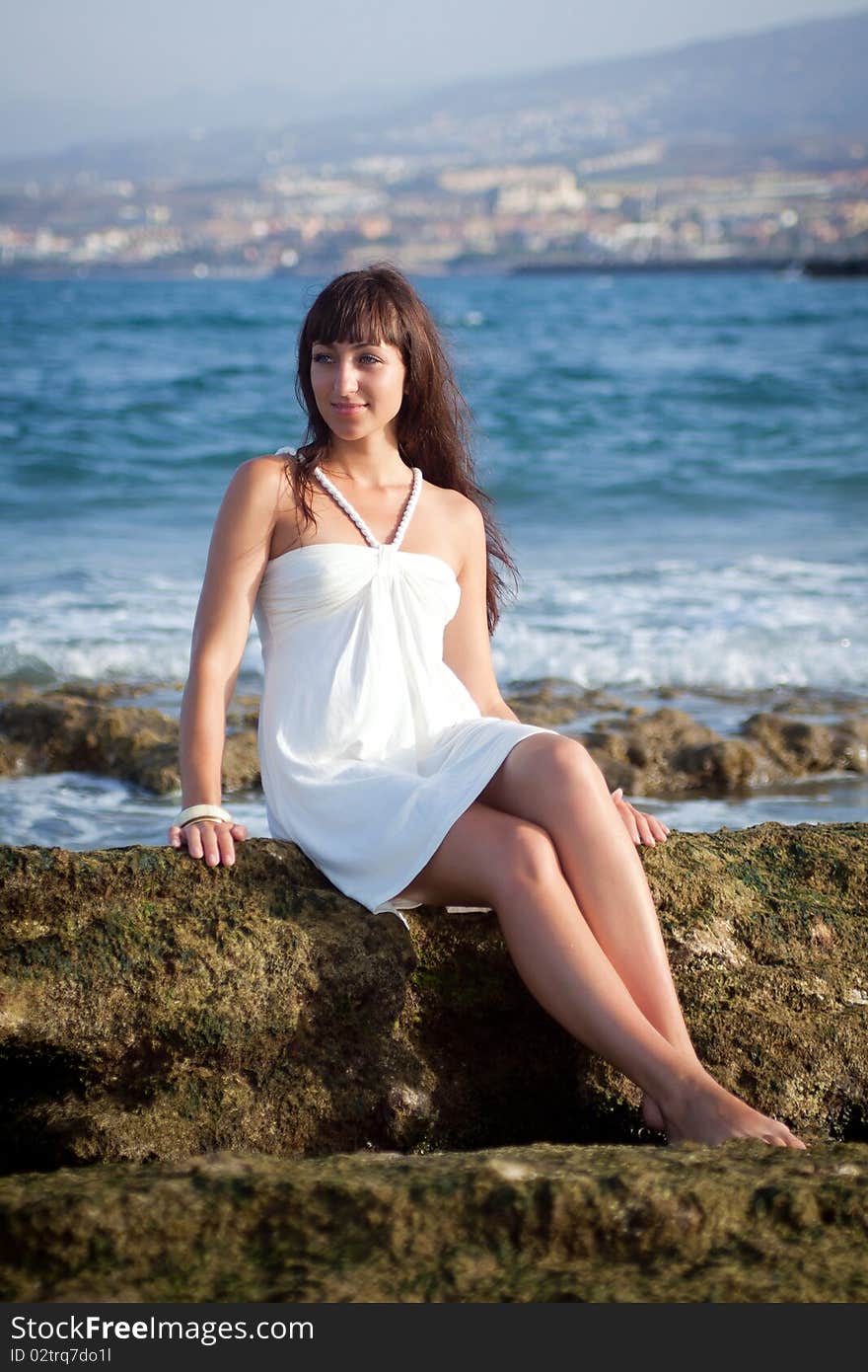 Pretty young female sitting on the rock in front of the ocean shore. Southern Tenerife, Atlantic Ocean. Pretty young female sitting on the rock in front of the ocean shore. Southern Tenerife, Atlantic Ocean.