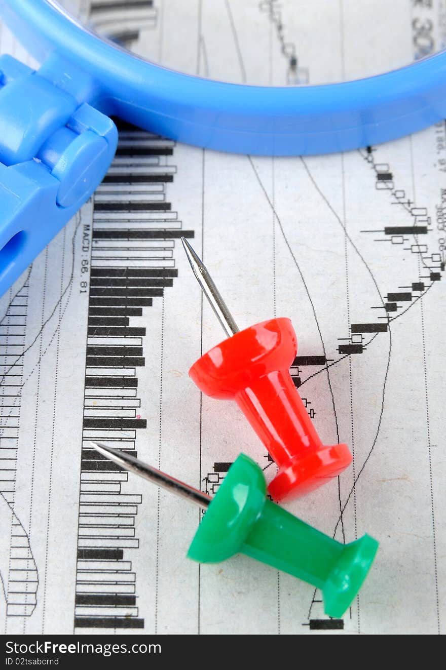 A blue magnifier and drawing pin in red and green color, putting on a stock graph, means business and finance analysis and key point. A blue magnifier and drawing pin in red and green color, putting on a stock graph, means business and finance analysis and key point.