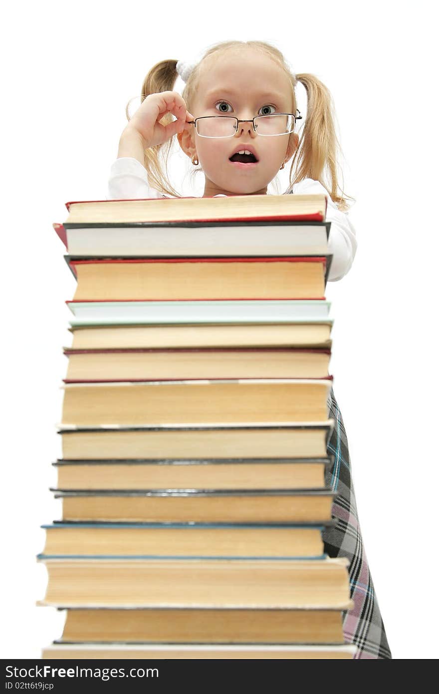 Cute funny little schoolgirl standing behind the books with glasses on studio shot on white background