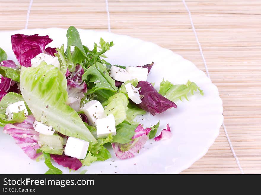 Leafs salad  with sheep cheese on plate,closed-up on wooden mat