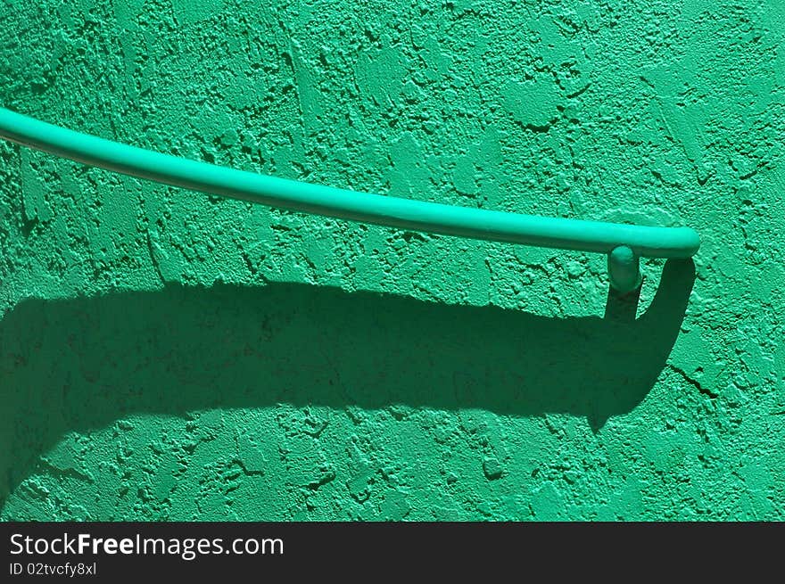 A green handrail with shadow arcs diagonally along a textured green wall. A green handrail with shadow arcs diagonally along a textured green wall.