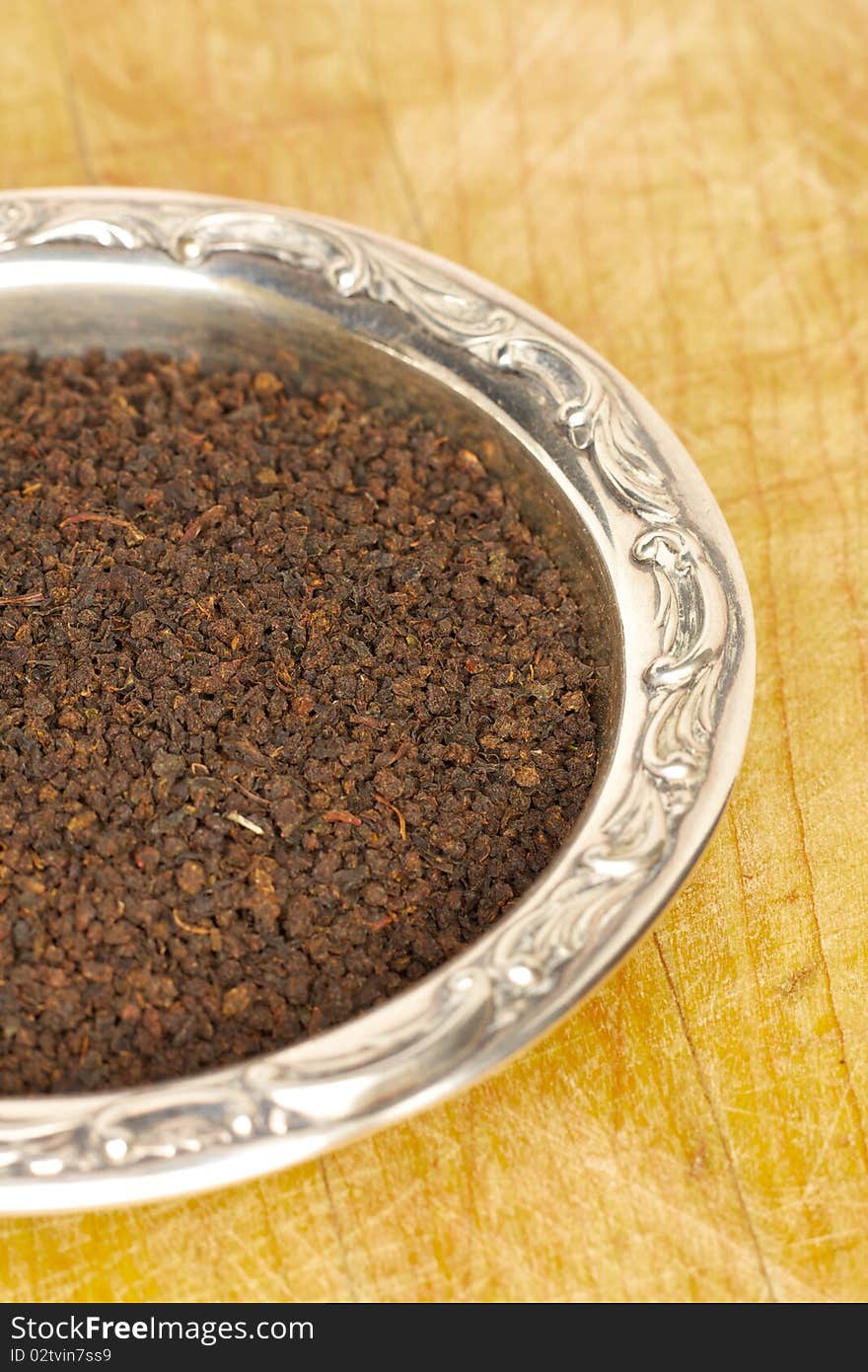 Loose black tea leaves in a sterling silver dish on a wooden surface. Loose black tea leaves in a sterling silver dish on a wooden surface