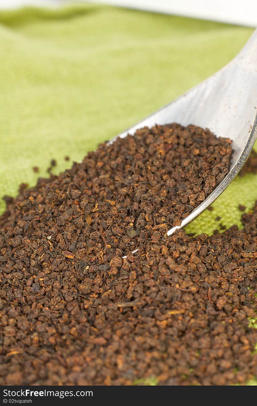 Loose black tea leaves spill from a spoon onto green linen