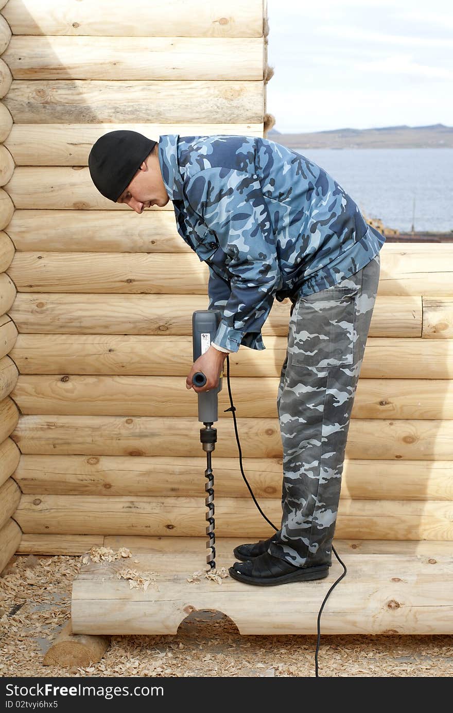 Carpenter drills a log on the construction of log cabin. Carpenter drills a log on the construction of log cabin