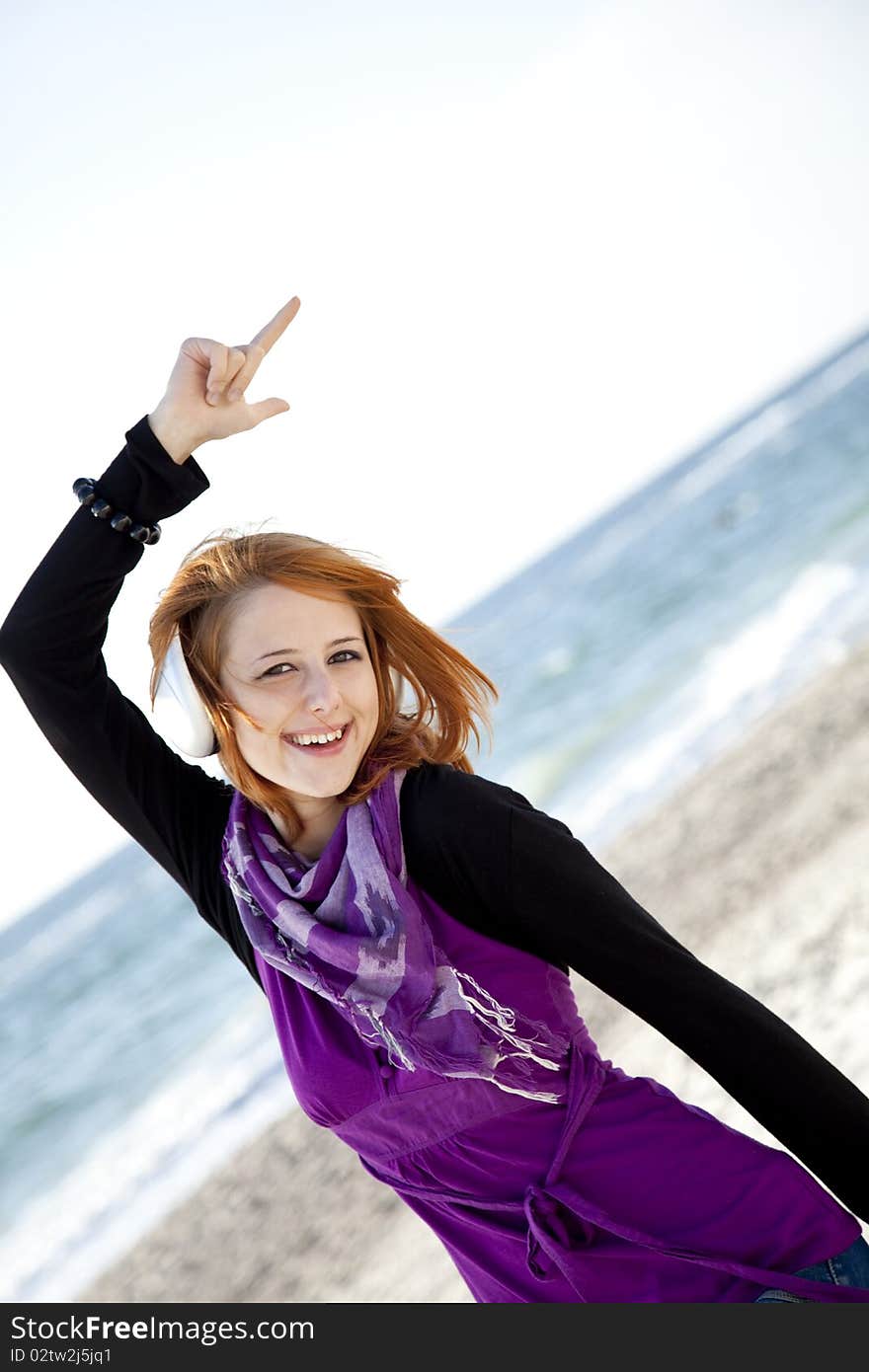 Red-haired girl in cap with headphone on the beach show OK symbol. Red-haired girl in cap with headphone on the beach show OK symbol.