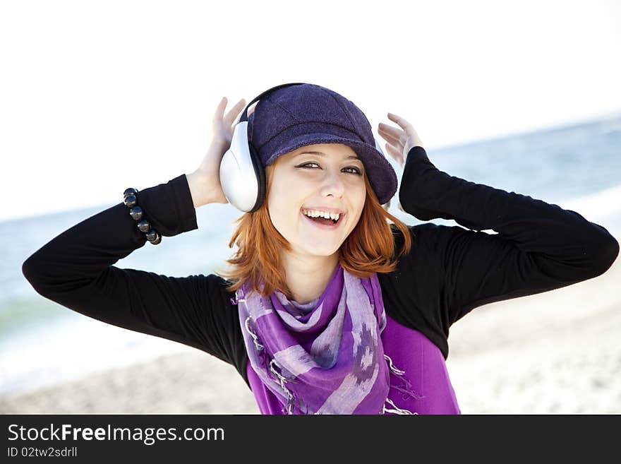 Red-haired girl in cap with headphone on the beach show OK symbol. Red-haired girl in cap with headphone on the beach show OK symbol.