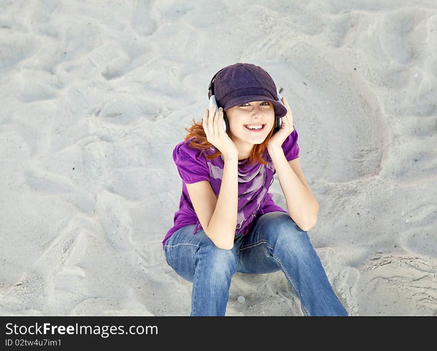 Portrait of red-haired girl with headphone on the beach.