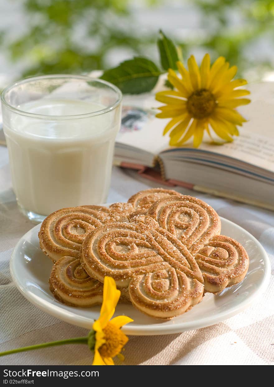 Glass of milk with two cookies. Book with flower on background. Glass of milk with two cookies. Book with flower on background