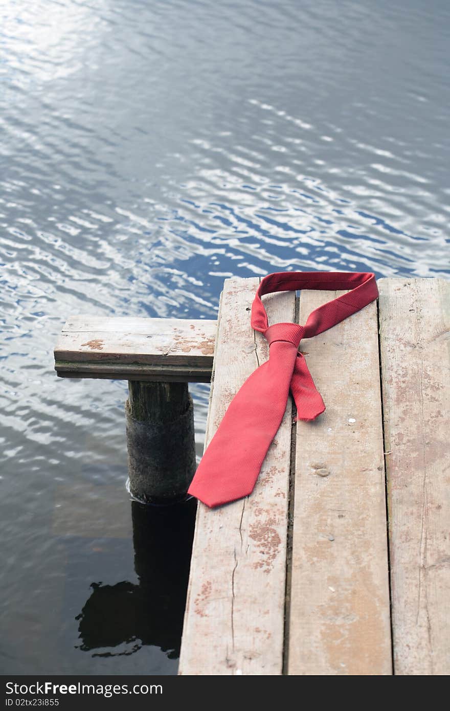 Concept with red necktie lying on wooden pier on background with river. Concept with red necktie lying on wooden pier on background with river