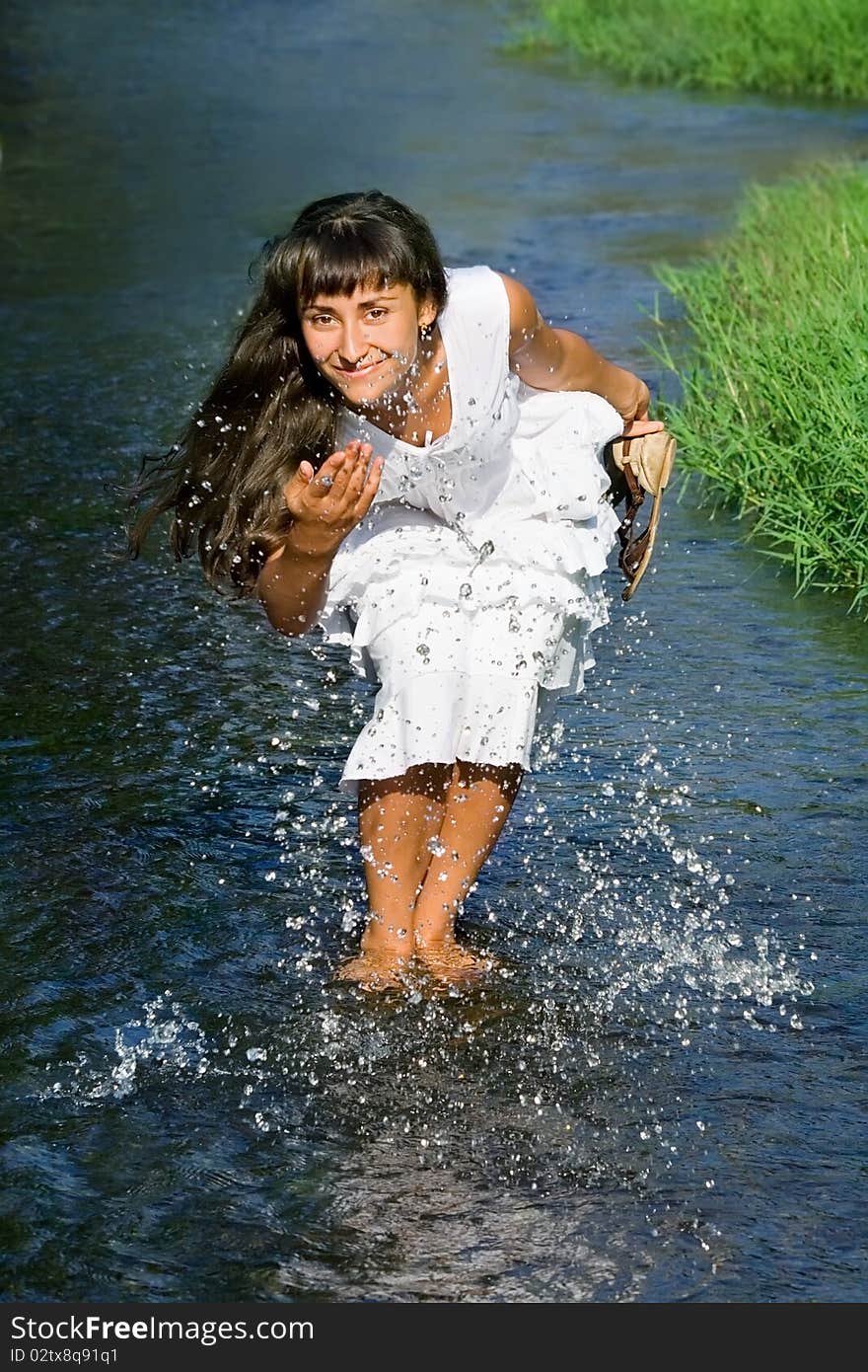 Young attractive  lady in white dress smiling and  splashing in the stream. Young attractive  lady in white dress smiling and  splashing in the stream