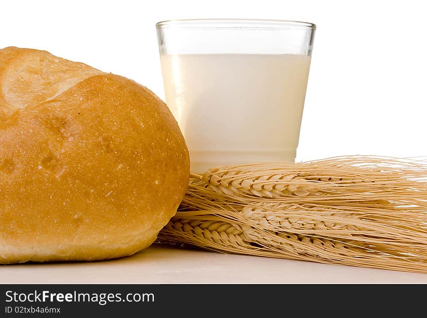 Milk in a glass with a white loaf and grain ears.