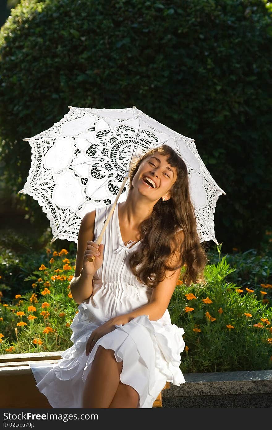 Happy attractive girl in white dress with sun umbrella sitting and laughing on the bench in the park. Happy attractive girl in white dress with sun umbrella sitting and laughing on the bench in the park