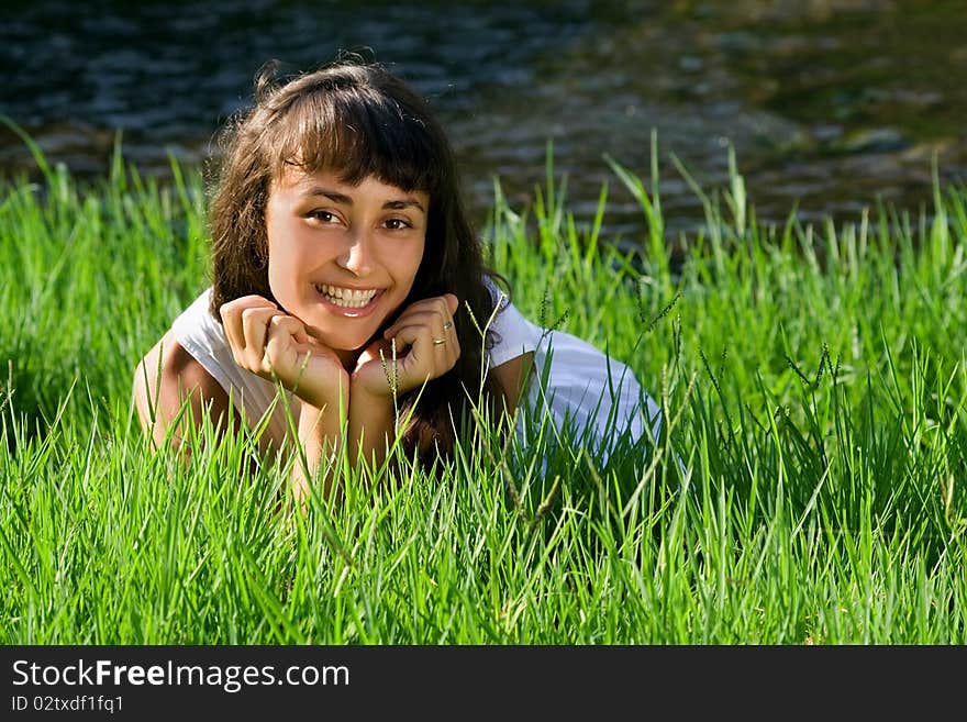 Young smiling girl liying on the fresh green grass near the river. Young smiling girl liying on the fresh green grass near the river