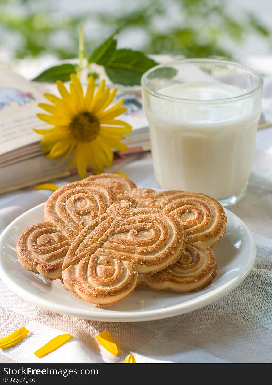 Glass of milk with two cookies. Book with flower on background. Glass of milk with two cookies. Book with flower on background