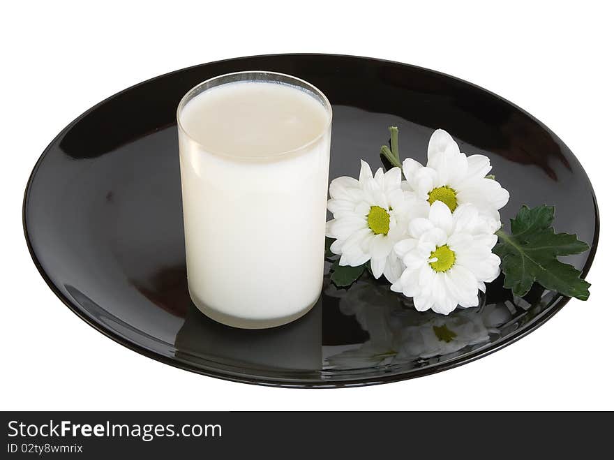 Glass of milk and white camomiles with reflection on a black dish