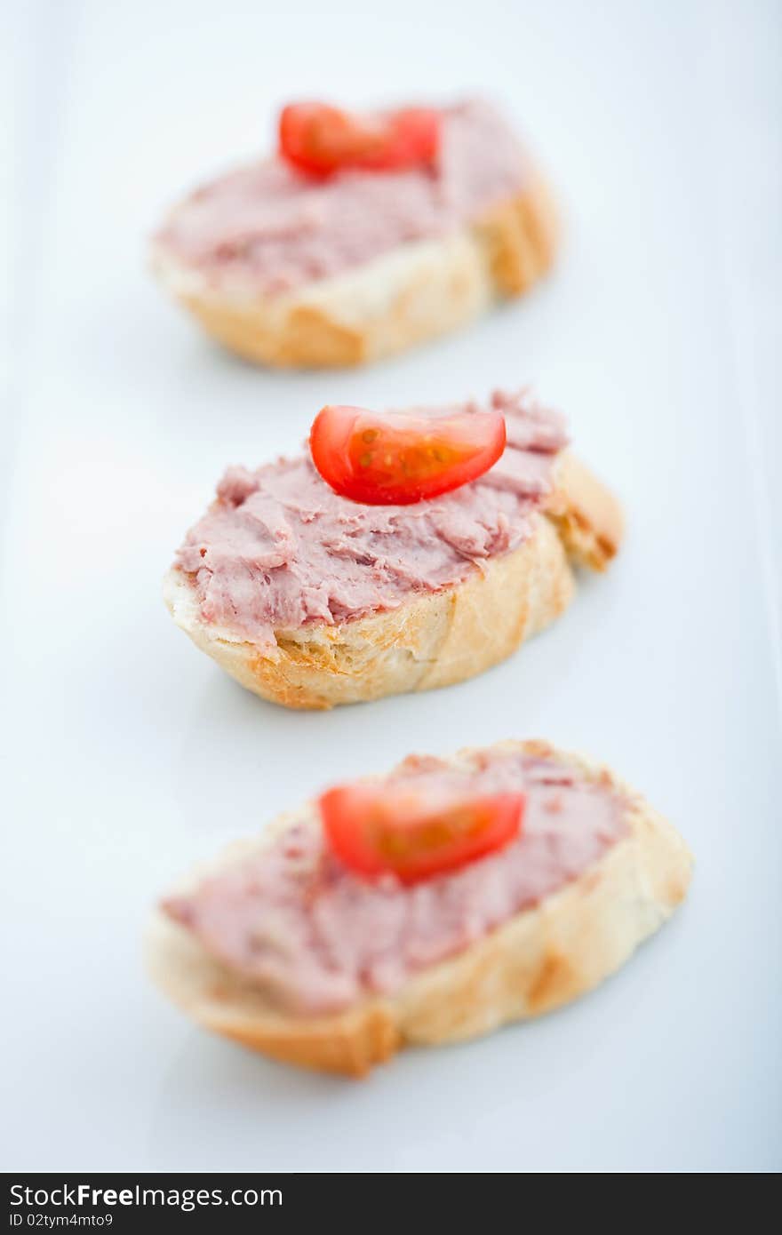 Three baguette slices with liver and apple pate and a thin tomato slice on top. Shallow DOF