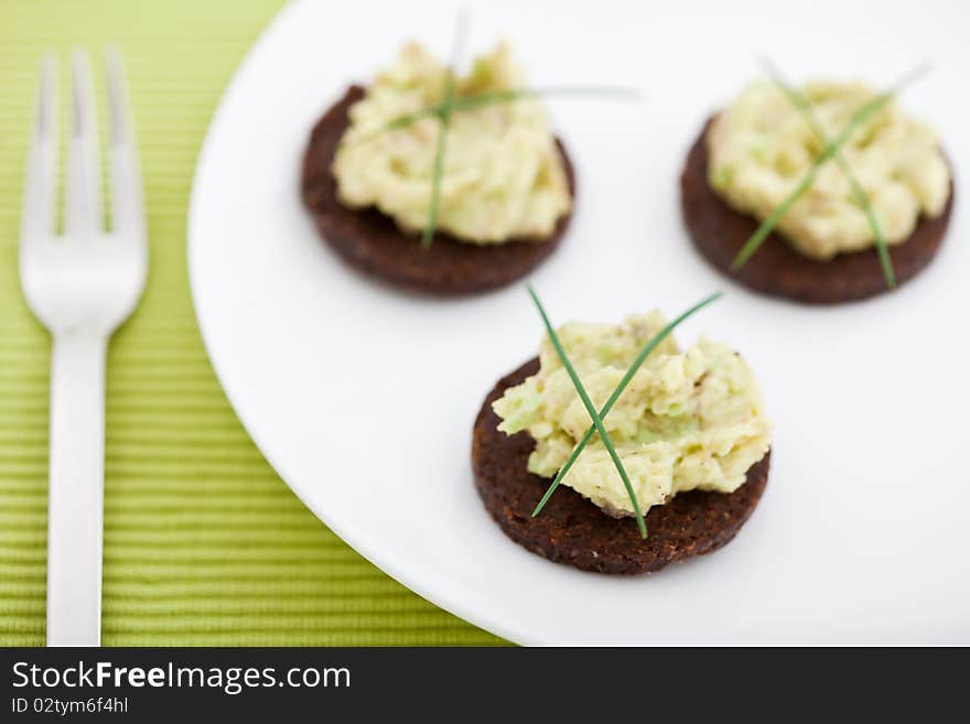 Three pumpernickel slices with guacamole on a white plate. Shallow DOF